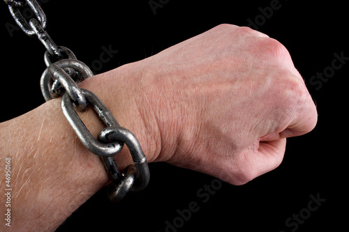 Photo: Hand in fist and shackles, black background Hand in fist and shackles, black background