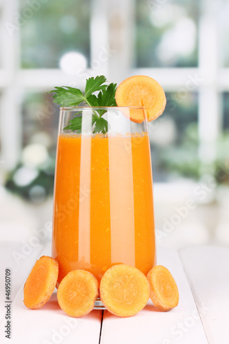Photo: Glass of carrot juice on wooden table, on window background Glass of carrot juice on wooden table, on window background