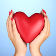 Red heart in woman's hands on color background