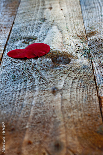Photo: Red heart shaped rose petal on rustic wooden table Red heart shaped rose petal on rustic wooden table