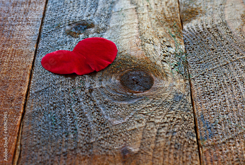 Photo: Red heart shaped rose petal on rustic wooden table Red heart shaped rose petal on rustic wooden table
