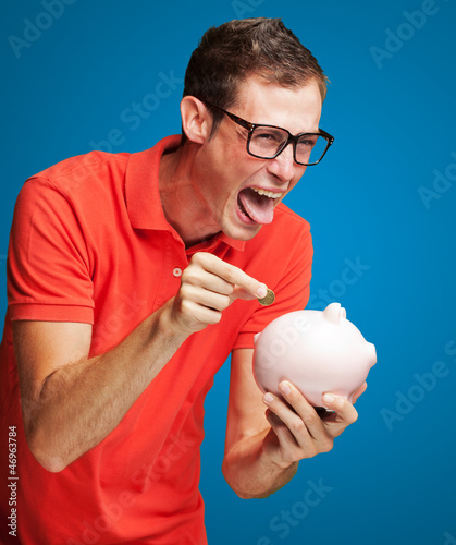 Photo: Portrait Of Man With Piggy Bank Inserting A Coin Portrait Of Man With Piggy Bank Inserting A Coin