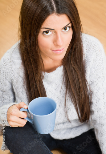 Photo: Woman sitting on the floor while looking up and holding a mug Woman sitting on the floor while looking up and holding a mug