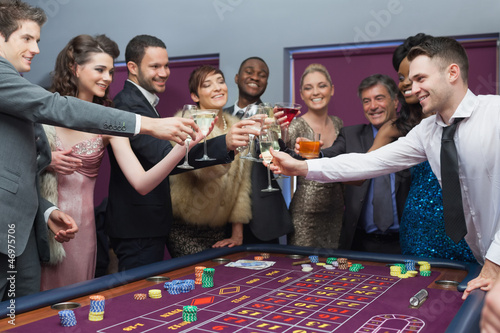 Photo: People standing clinking glasses at roulette table People standing clinking glasses at roulette table