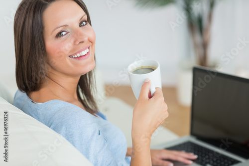 Photo: Brunette using her laptop and drinking a cup of coffee Brunette using her laptop and drinking a cup of coffee