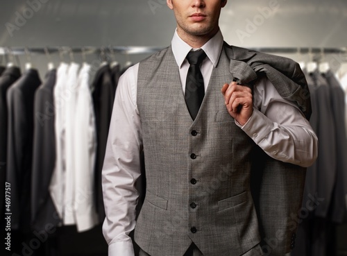Photo: Businessman in classic vest against row of suits in shop Businessman in classic vest against row of suits in shop