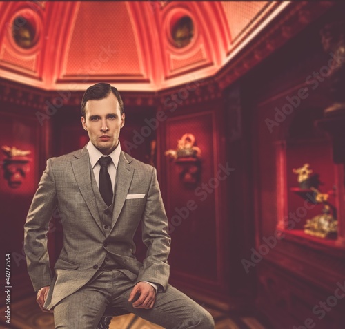 Photo: Confident man in classic grey suit sitting on chair in cabinet Confident man in classic grey suit sitting on chair in cabinet