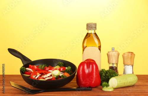Photo: frying pan with vegetables on yellow background frying pan with vegetables on yellow background