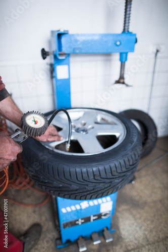 Photo: Auto mechanic in a garage checking the air pressure in a tyre Auto mechanic in a garage checking the air pressure in a tyre