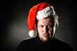 Portrait of angry man wearing santa hat against dark background.