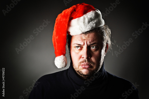 Photo: Portrait of upset man wearing santa hat against dark background. Portrait of upset man wearing santa hat against dark background.