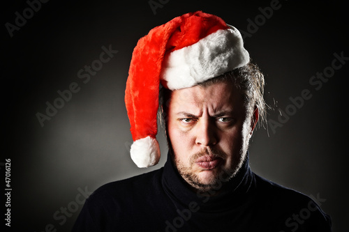 Photo: Portrait of angry man wearing santa hat against dark background. Portrait of angry man wearing santa hat against dark background.