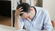 Middle-aged man at his desk holding his head while looking tired