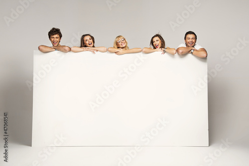 Photo: Happy joyful group of friends displaying white placard Happy joyful group of friends displaying white placard