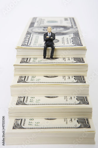 Photo: Businessman figurine sitting on stack of dollars Businessman figurine sitting on stack of dollars