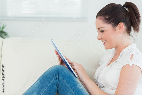 Photo: Happy woman using a tablet pc and sitting on the couch Happy woman using a tablet pc and sitting on the couch