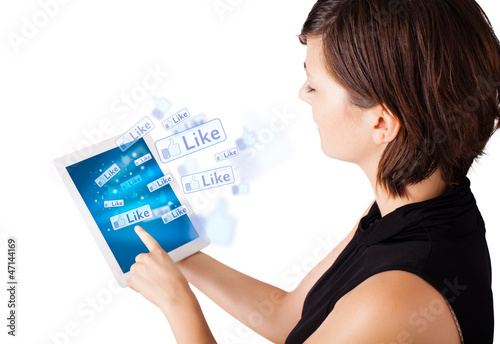 Photo: Young woman looking at modern tablet with social icons Young woman looking at modern tablet with social icons