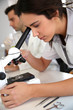 Young woman looking through microscope lense
