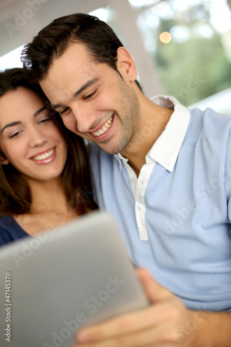 Photo: Smiling couple websurfing on internet with tablet Smiling couple websurfing on internet with tablet