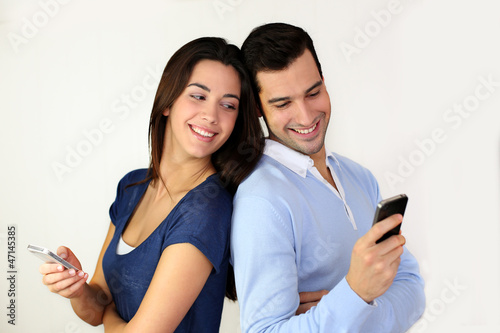 Photo: Couple standing back to back and using smartphone Couple standing back to back and using smartphone