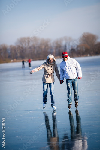 Photo: Couple ice skating outdoors on a pond on a lovely sunny winter d Couple ice skating outdoors on a pond on a lovely sunny winter d