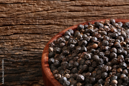 Photo: Bowl with black pepper over a wooden background Bowl with black pepper over a wooden background