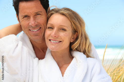 Photo: Happy couple wearing dressing gowns at the beach Happy couple wearing dressing gowns at the beach