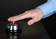 Hand ringing in service bell on wooden table on black