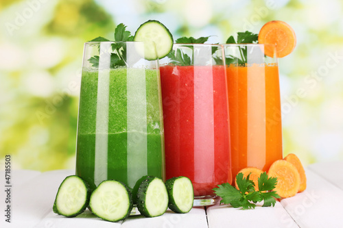 Photo: Fresh vegetable juices on wooden table, on green background Fresh vegetable juices on wooden table, on green background