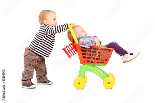 Photo: Toddler boy pushing his twin sister in a toy cart Toddler boy pushing his twin sister in a toy cart
