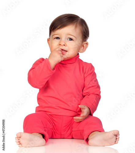 Photo: Adorable baby girl with her hand in mouth sitting Adorable baby girl with her hand in mouth sitting
