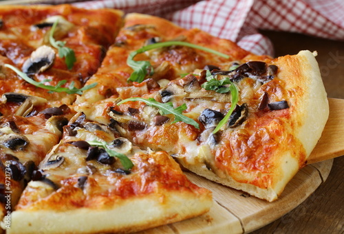 Photo: Italian pizza with mushrooms and olives on a wooden board Italian pizza with mushrooms and olives on a wooden board