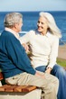 Senior Couple Sitting On Bench By Sea Together