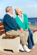 Senior Couple Sitting On Bench By Sea Together