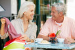 Senior Couple Enjoying Snack At Outdoor Café After Shopping