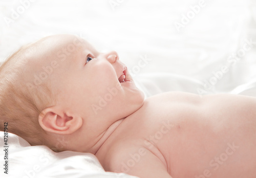 Foto: Cute adorable baby girl lying down and smiling isolated on white Cute adorable baby girl lying down and smiling isolated on white