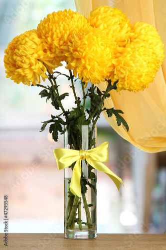 Photo: bright yellow chrysanthemums in glass vase, on wooden table bright yellow chrysanthemums in glass vase, on wooden table