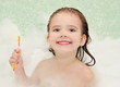 Smiling little girl is taking a bath holding toothbrush