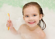 Smiling little girl is taking a bath holding toothbrush