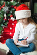 Girl in Santa hat sits and writes letter to Santa