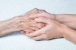A young girl holds hands of an old man. Closeup.