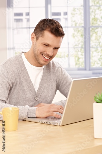 Photo: Young man using laptop at home Young man using laptop at home