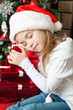 Happy girl in Santa hat with gifts sleeping near christmas tree