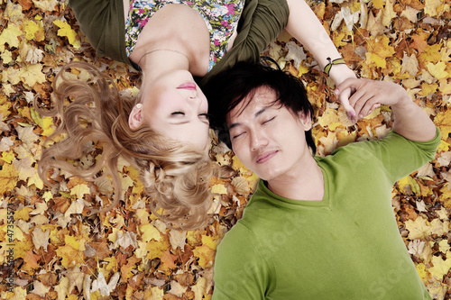Photo: Beautiful loving couple sleep on autumn leaves Beautiful loving couple sleep on autumn leaves