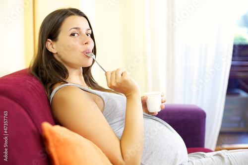 Photo: Happy pregnant woman licking spoong with yogurt Happy pregnant woman licking spoong with yogurt