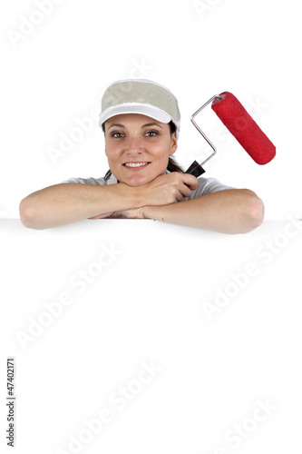 Photo: Woman stood by blank poster with paint roller Woman stood by blank poster with paint roller