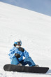 Snowboarder in ski suit and helmet sits on snowy hillside