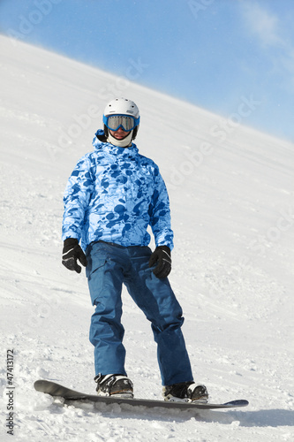 Photo: Snowboarder in ski suit and helmet stands on snowboard Snowboarder in ski suit and helmet stands on snowboard