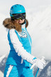 Young smiling woman inski suit poses against snowy mountain