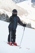 Boy skier in ski suit and helmet stands on snowy slope